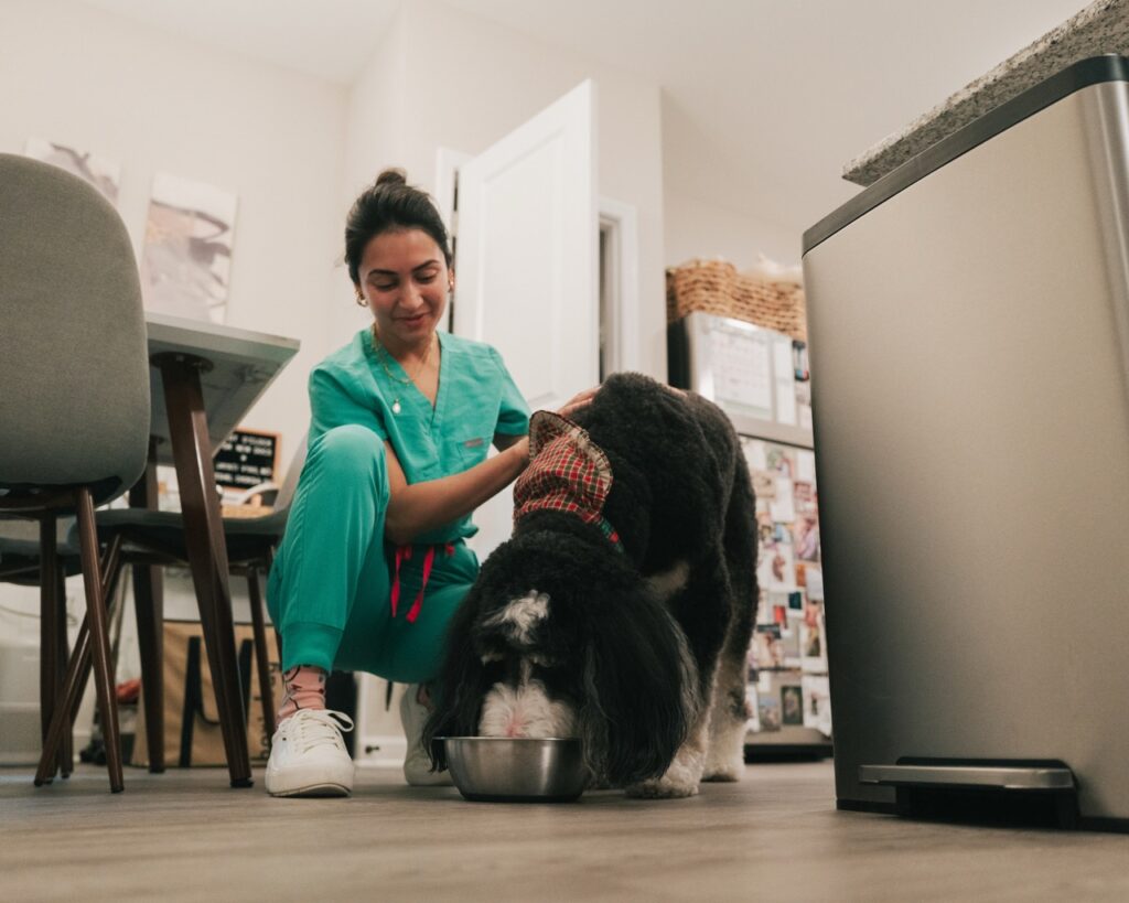 Woman kneeling next to a dog who is eating out of a bowl